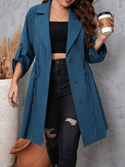 Dusty blue trench coat with gathered waistline, roll-up sleeves, and tie detail.