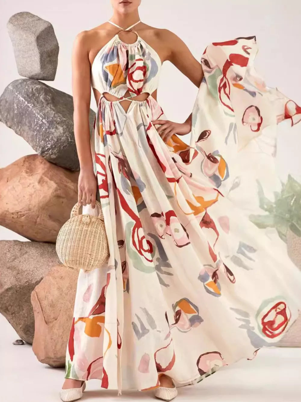 Abstract print halter maxi dress with cut-outs on a cream background, featuring colorful floral motifs.