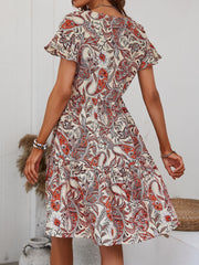 Paisley print mini dress in cream with orange and red details, flutter sleeves, and tiered skirt.
