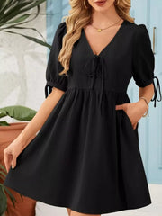 Black mini dress with tie neck, puff sleeves, and pockets.