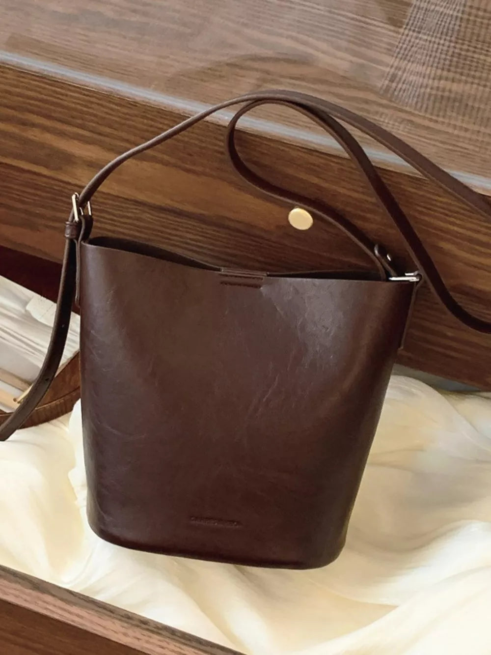 Distressed vintage bucket crossbody bag in brown leather with adjustable strap and gold snap closure.