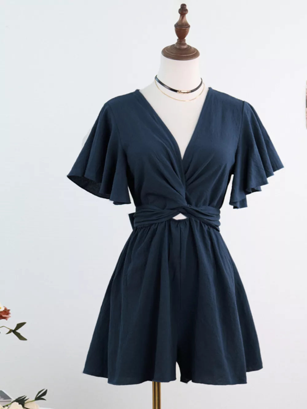 Navy blue cotton romper with flutter sleeves, V-neck, and tie-waist detail.