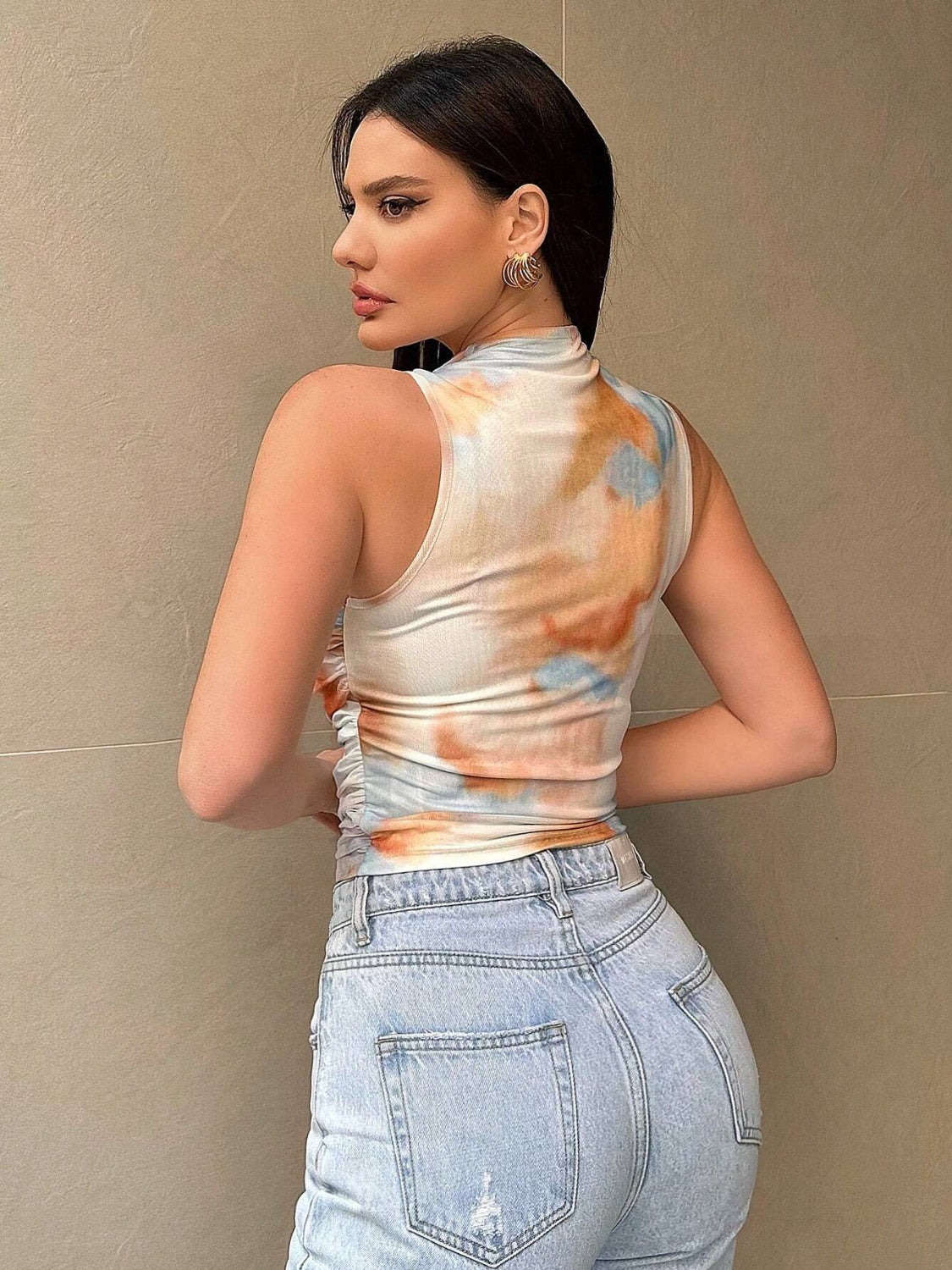 Sleeveless mock neck top with tie-dye pattern in white, orange, and blue, featuring ruched sides.