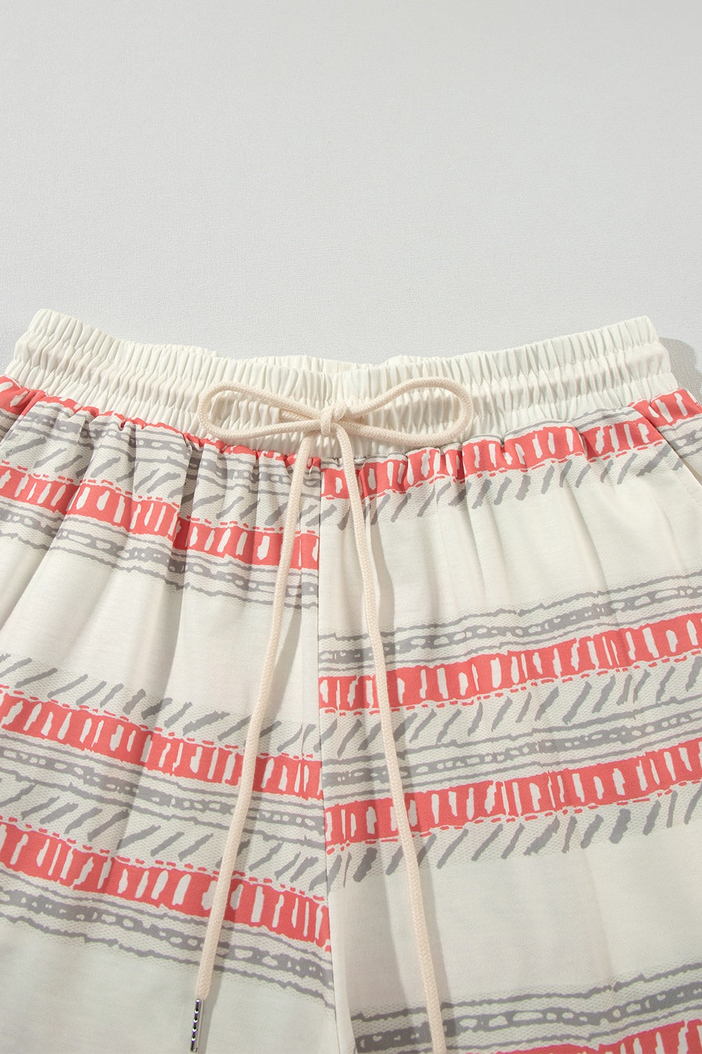 Ivory knit drawstring shorts with coral and grey abstract stripe pattern.
