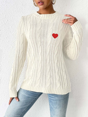 White cable knit sweater with embroidered red heart detail.