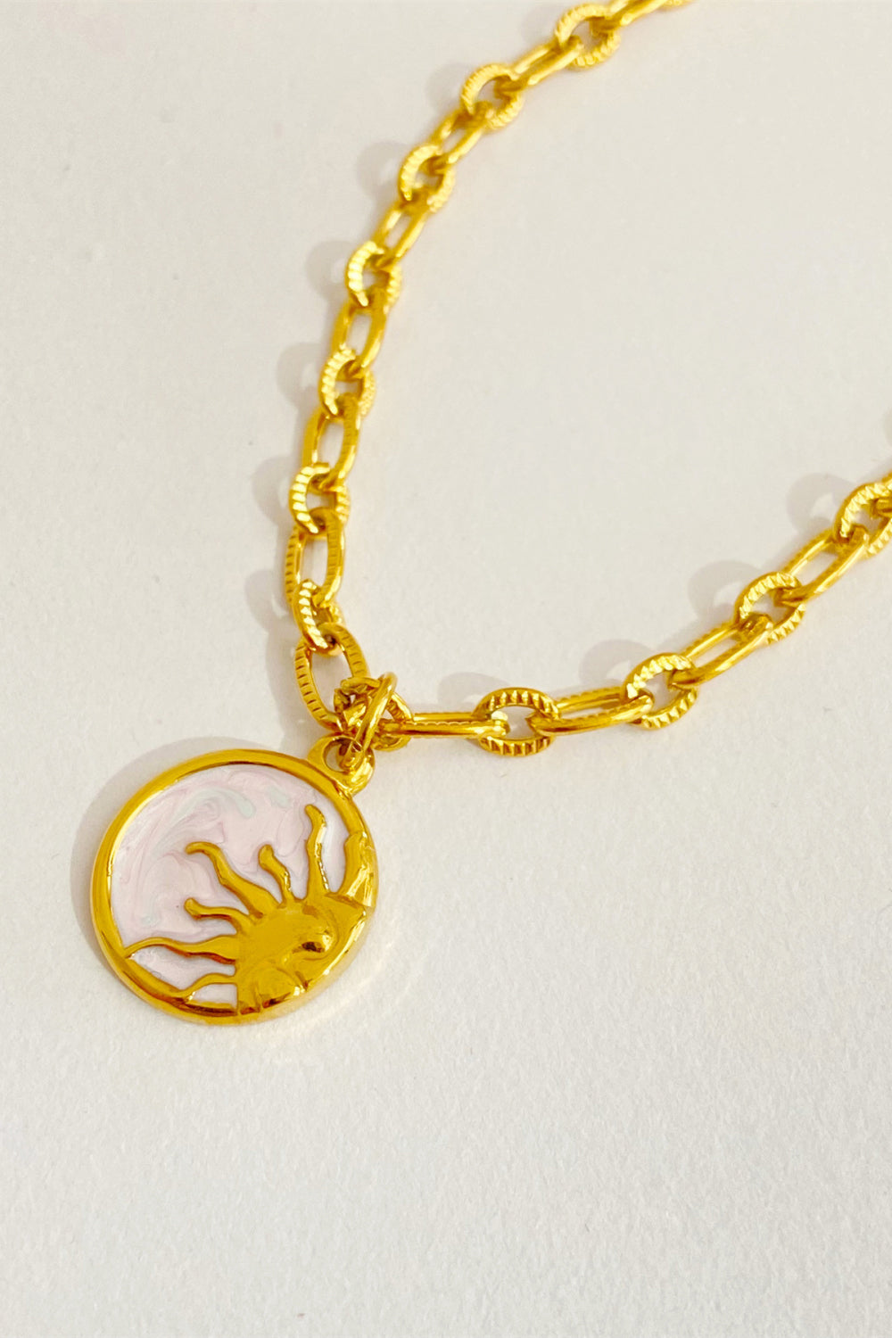 Celestial charm necklace in 18K gold-plated metal with a sun pendant and white enamel detail.