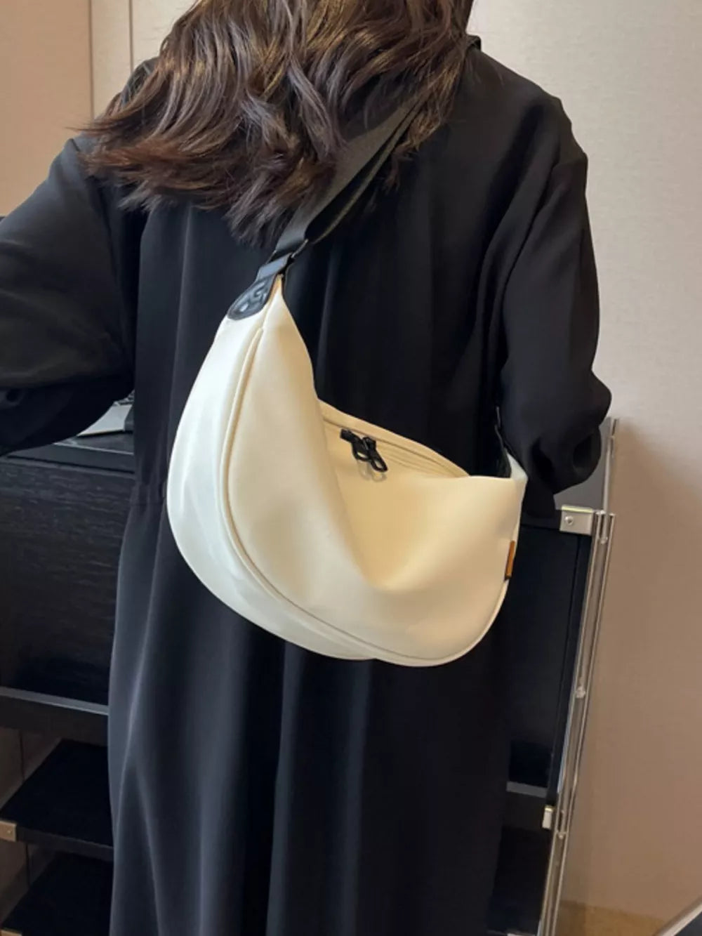 White crescent crossbody bag with adjustable strap and zipper closure.