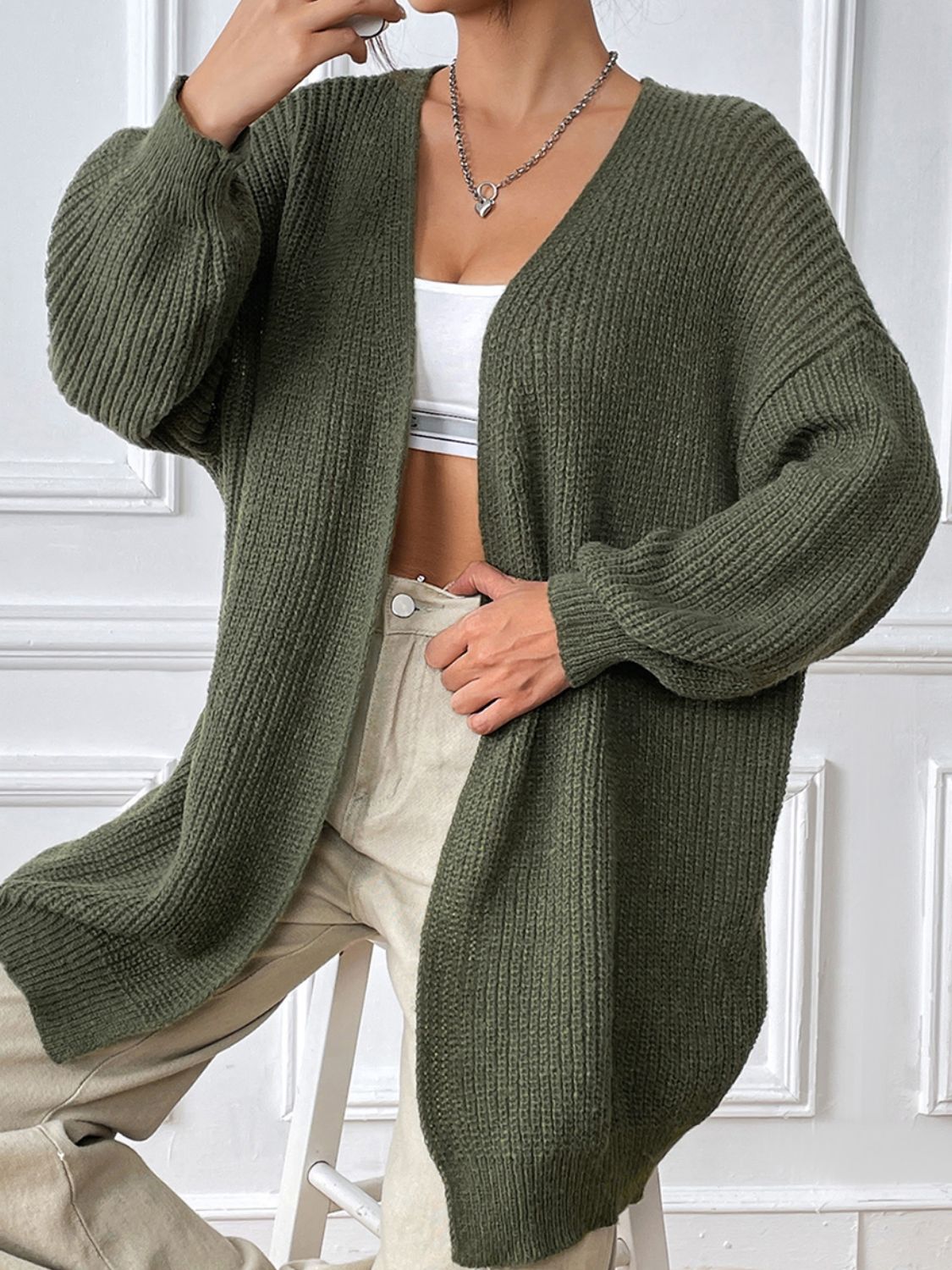 Olive green ribbed knit cardigan with balloon sleeves and a V-neck, styled open over a white top.