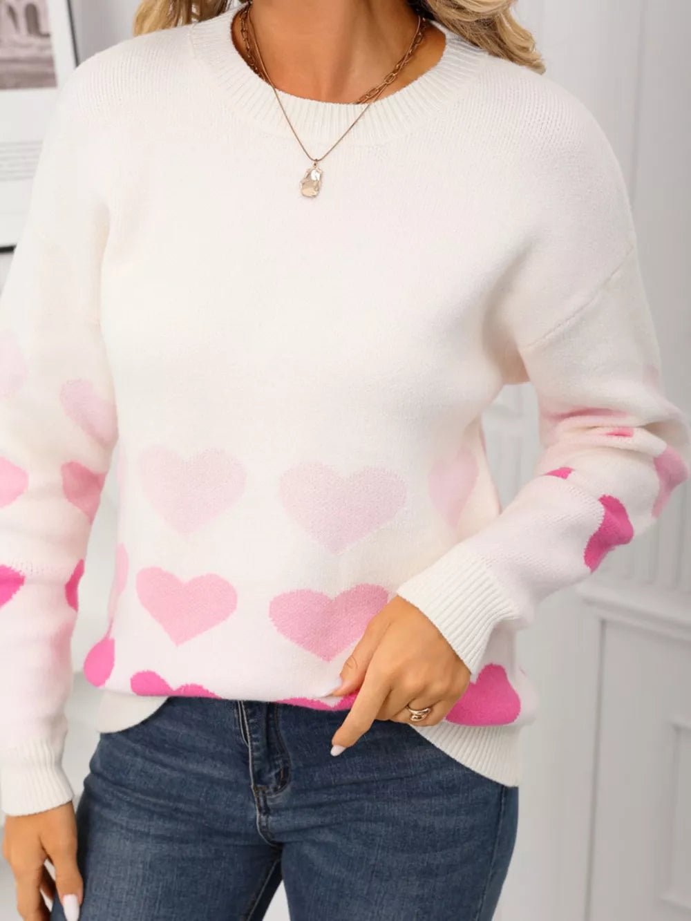 White crew neck sweater with pink heart print, acrylic knit, long sleeves.