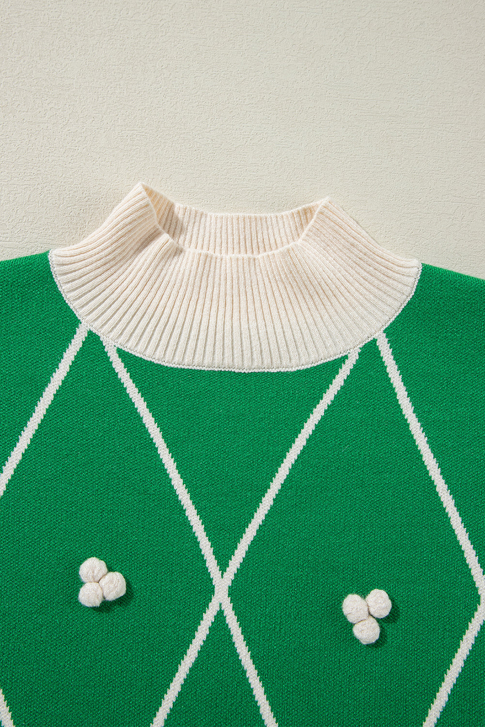 Dark green argyle knit sweater with mock neck and white pom embellishments.