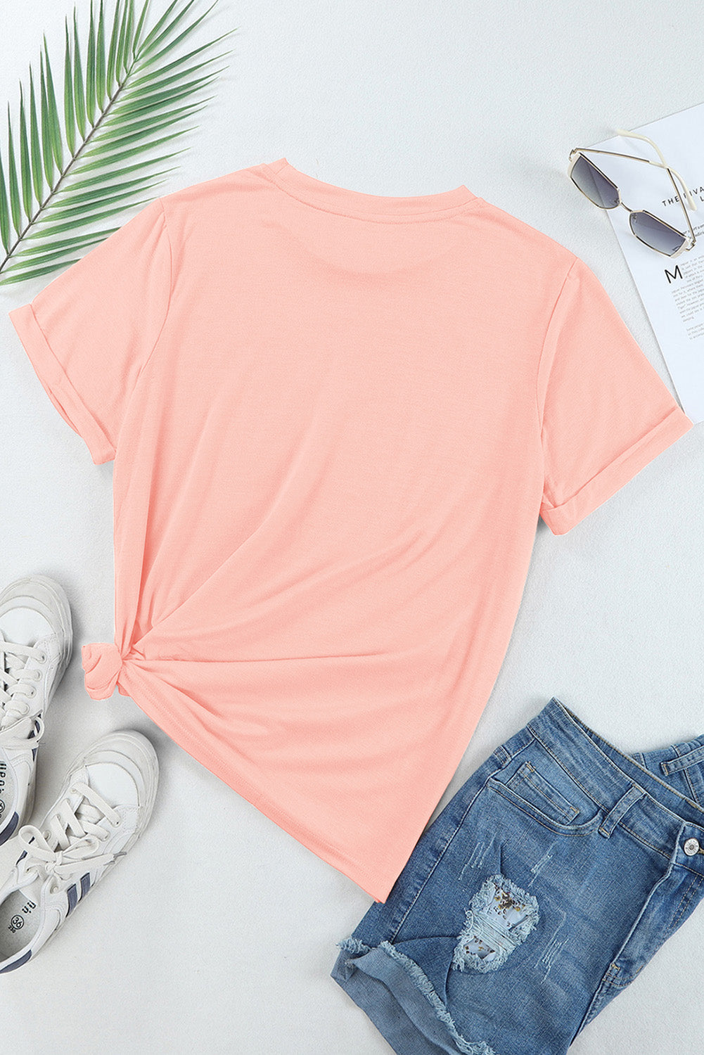 Watermelon pink graphic tee with rolled sleeves and a knotted hem, styled with denim shorts and sneakers.