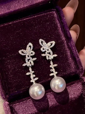 White pearl drop earrings with crystal butterfly details in a jewelry box.