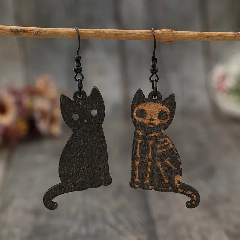Black laser-cut cat earrings, one solid silhouette, one with skeleton detail.