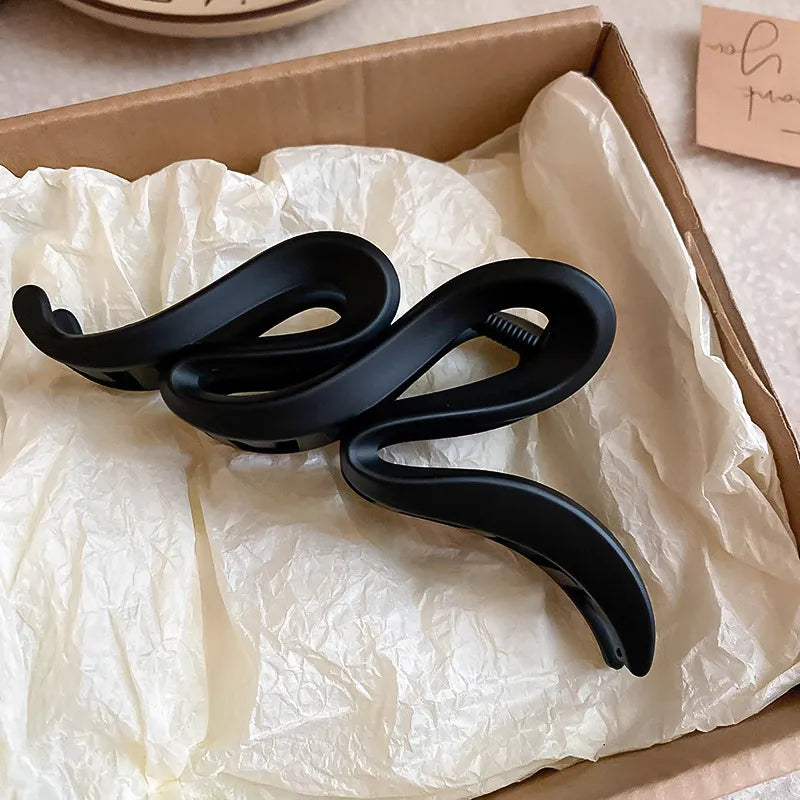 Black sculptural hair claw with serpentine design, matte acrylic material.
