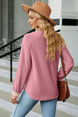 Pink textured V-neck blouse with embroidered cuffs and long sleeves.