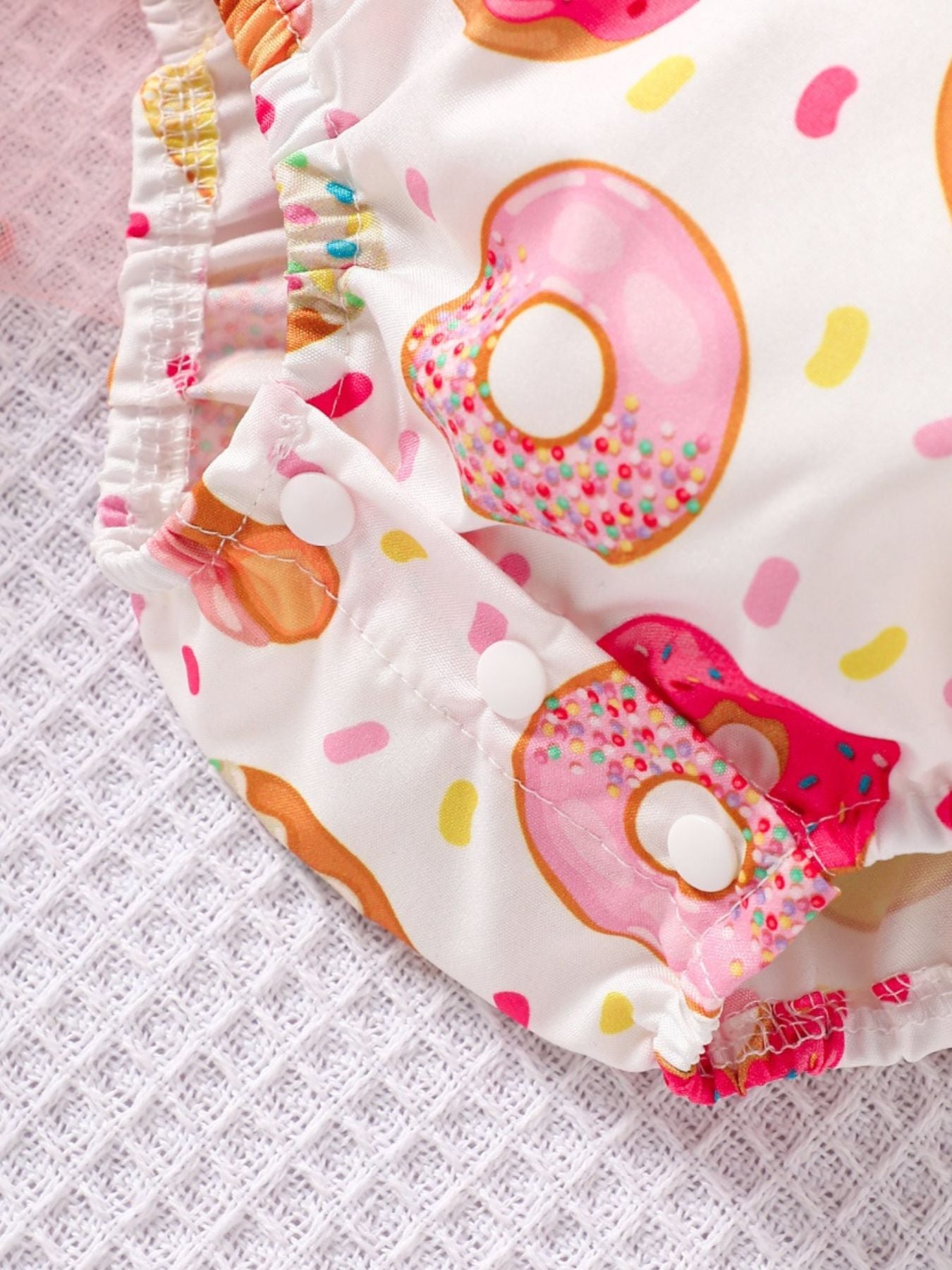 Baby cotton one-piece with donut print, smocked details, and snap closures.