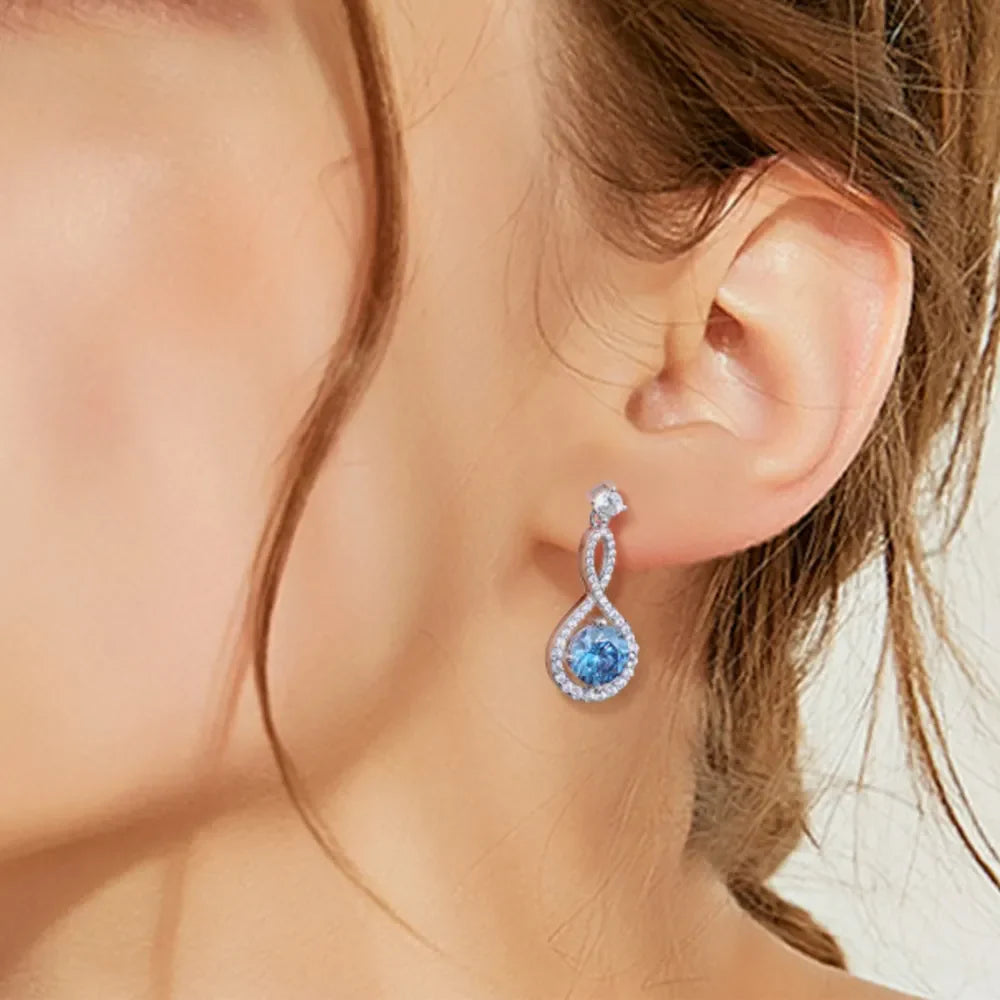 Infinity drop aquamarine earrings with white accents and a twisted silver design.