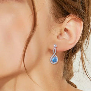 Infinity drop aquamarine earrings with white accents and a twisted silver design.