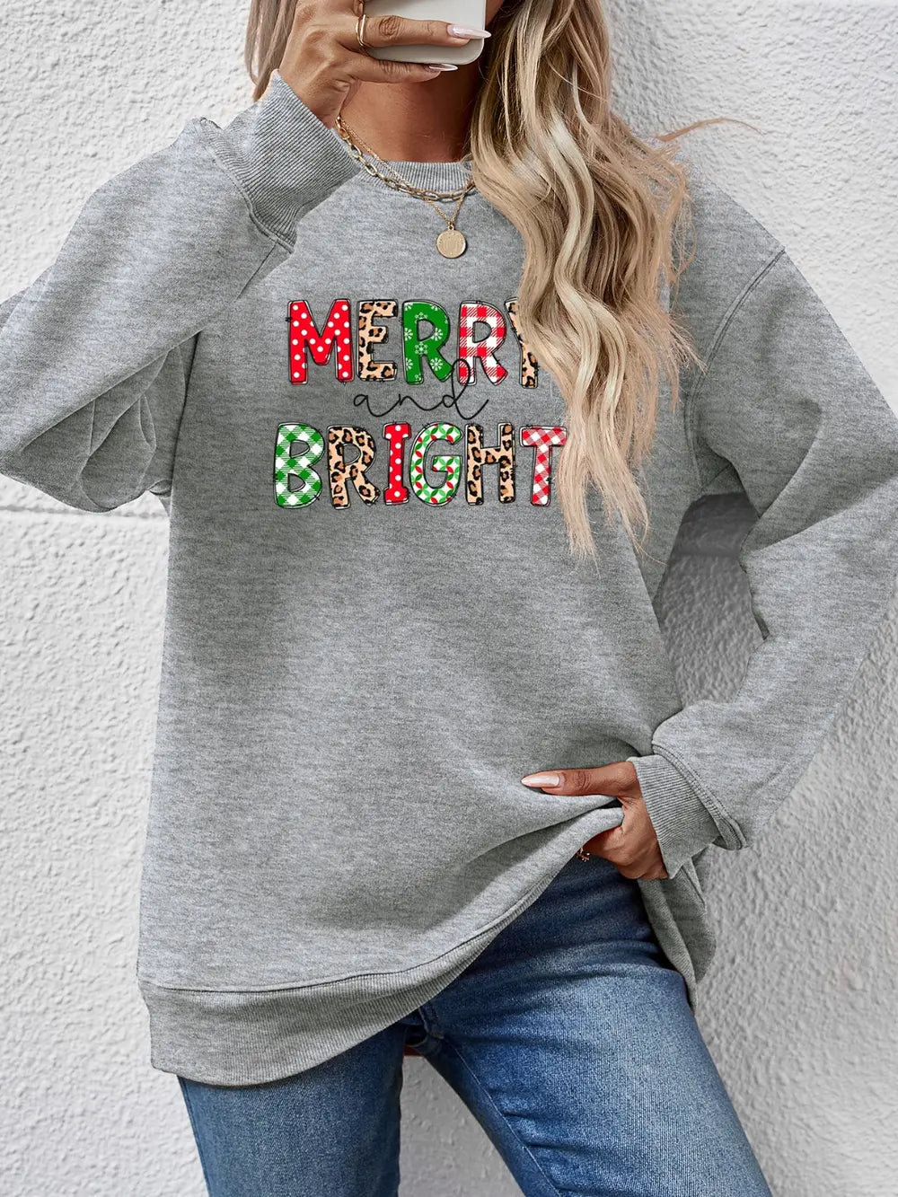 Gray sweatshirt with "Merry and Bright" graphic in festive patterns like polka dot, plaid, and leopard print.