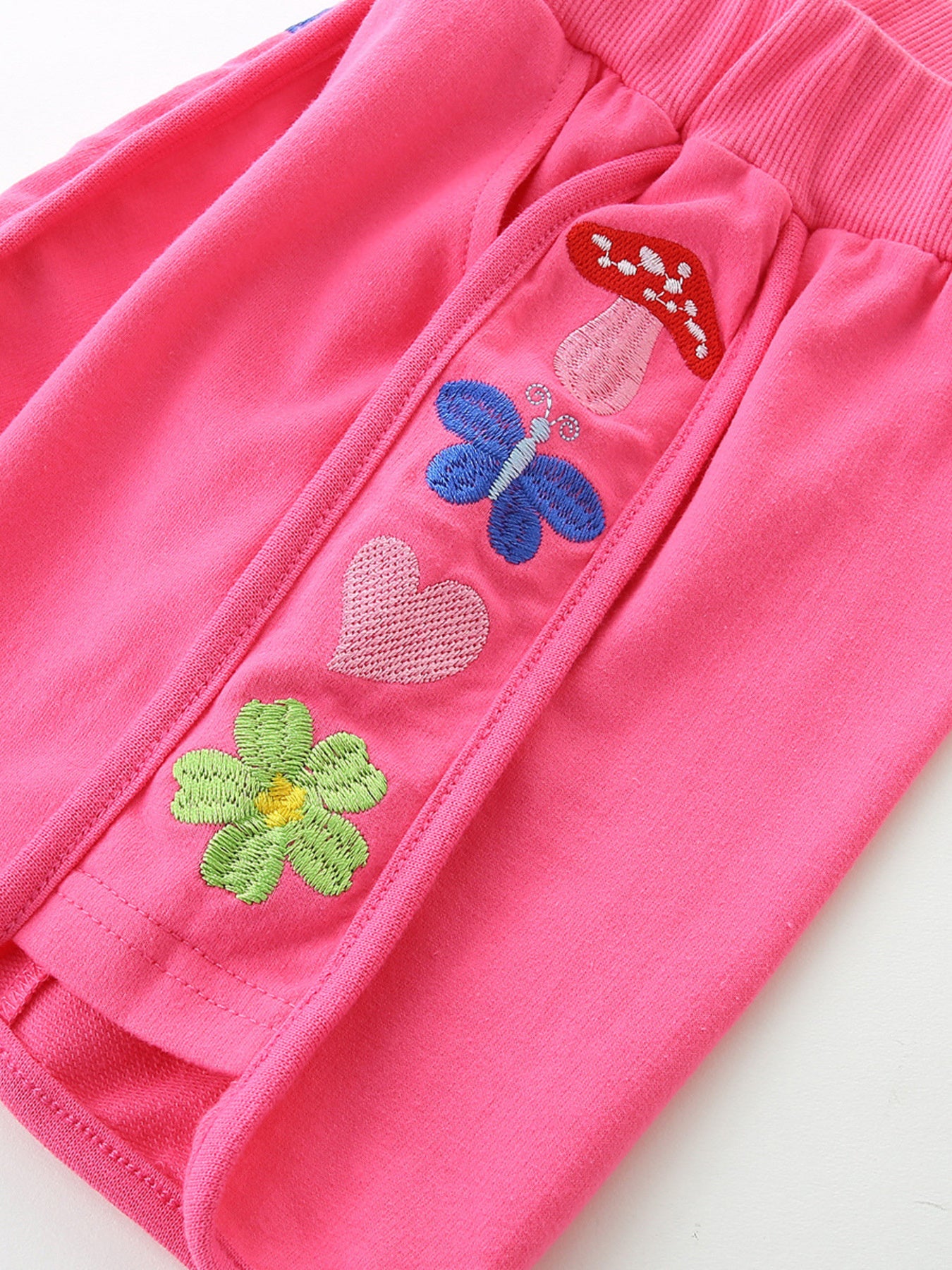 Pink toddler shorts with embroidered mushroom, butterfly, heart, and flower appliques.