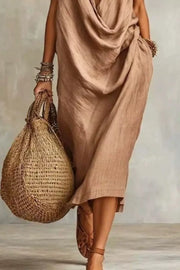 Tan midi dress with cowl neck and pockets, worn with sandals and a straw bag.