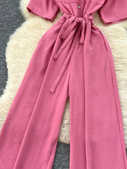 Pink belted wide-leg maternity jumpsuit with pockets and button detail.
