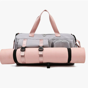 Gray gym duffel bag with pink straps and buckle details, holding a pink yoga mat.