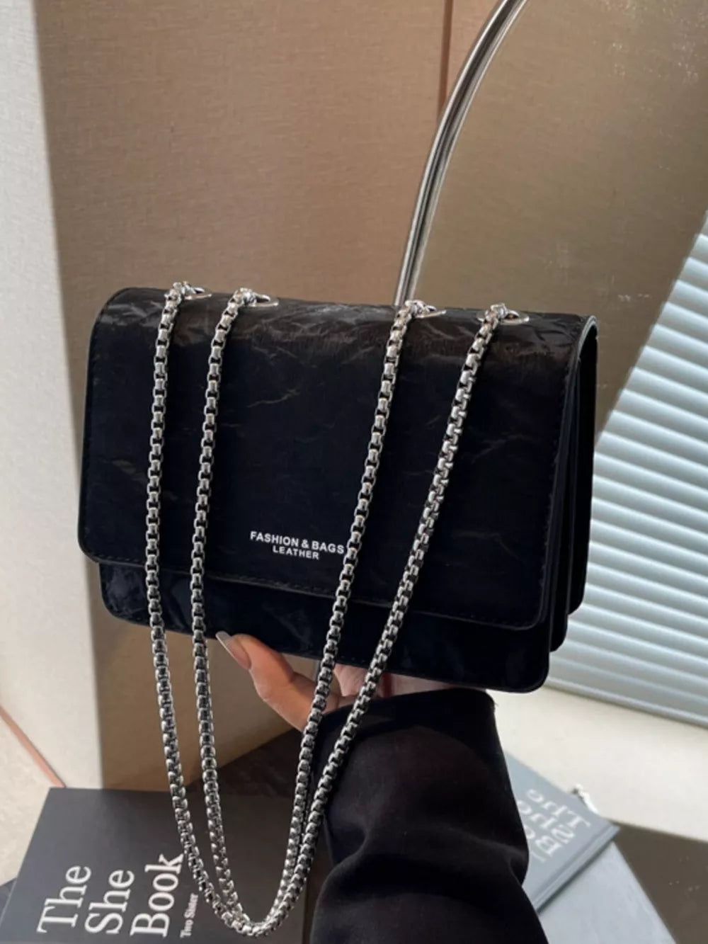 Black crumpled texture mini shoulder bag with silver chain strap and embossed text.