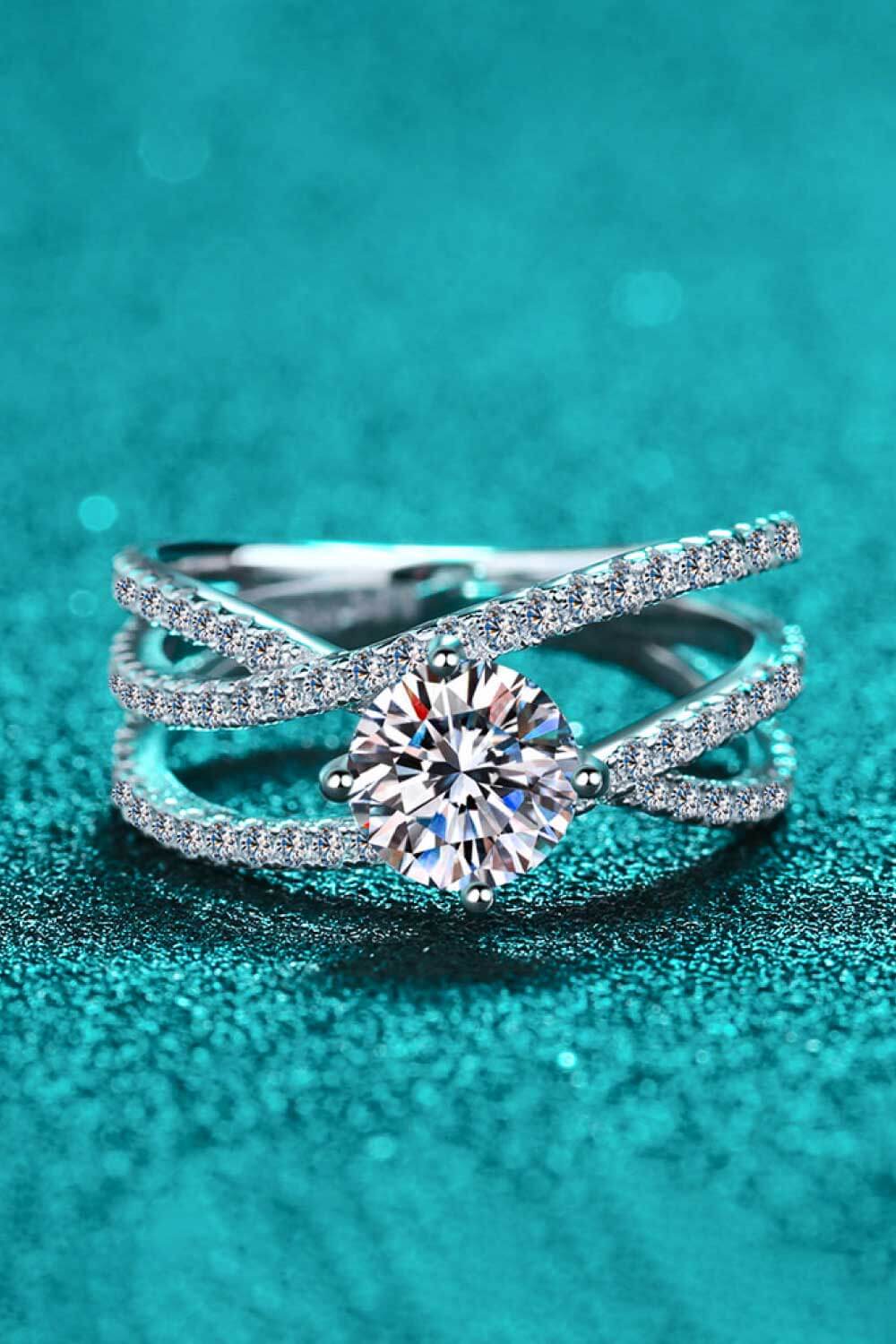 Silver crossover engagement ring with pavé-set band and round-cut center stone.