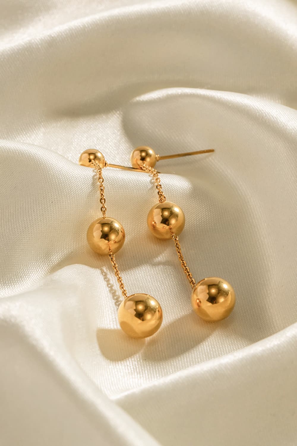 Gold triple orb drop earrings with delicate chains and a bold design.