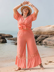 Coral viscose jumpsuit with lace sleeves and hem, tie-front top, and wide-leg pants.