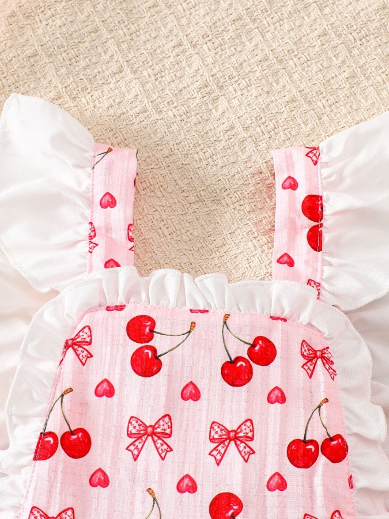 Pink baby dress with cherry print, ruffle trim, and white flutter sleeves.