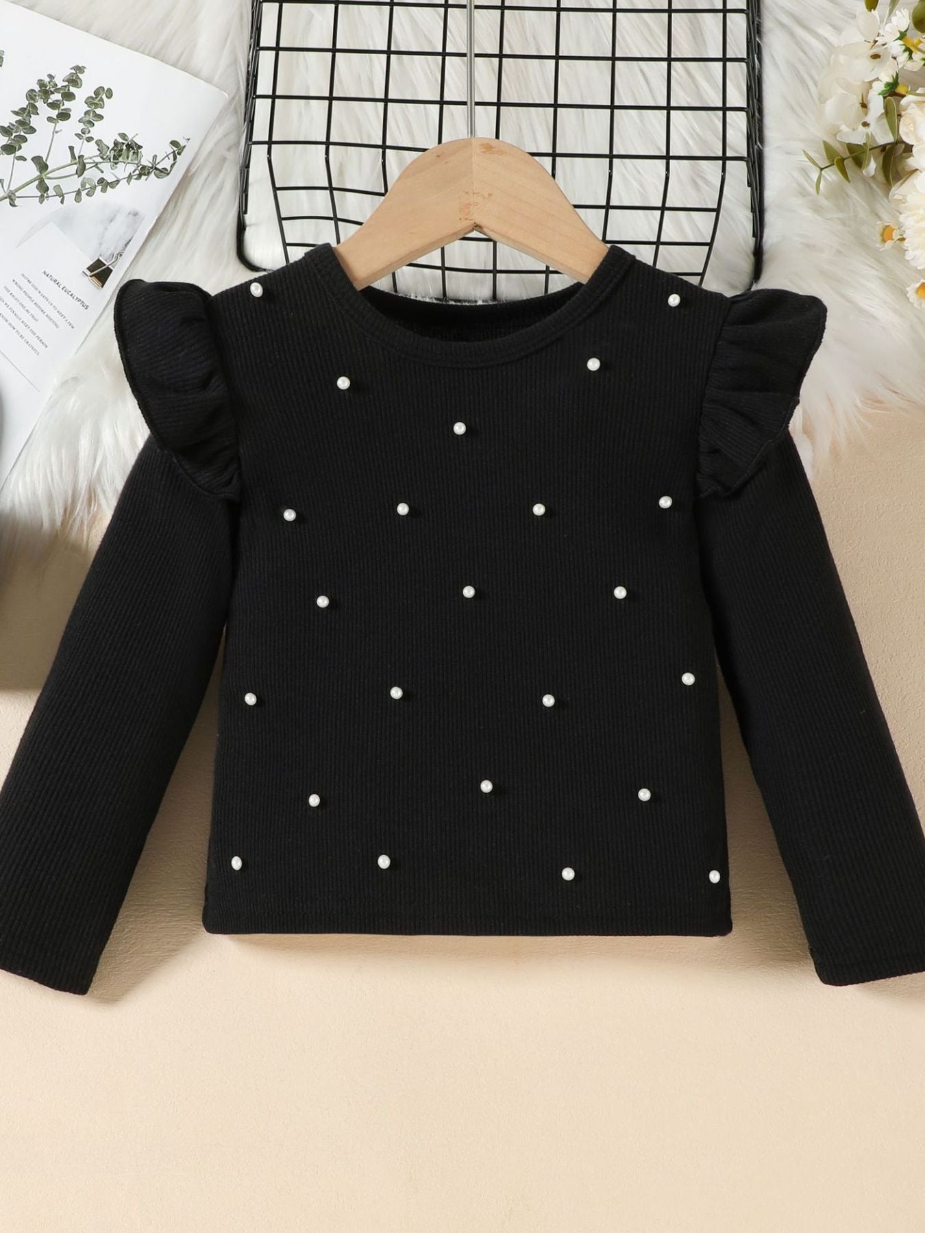 Toddler black ribbed long sleeve top with pearl embellishments and ruffled shoulders.