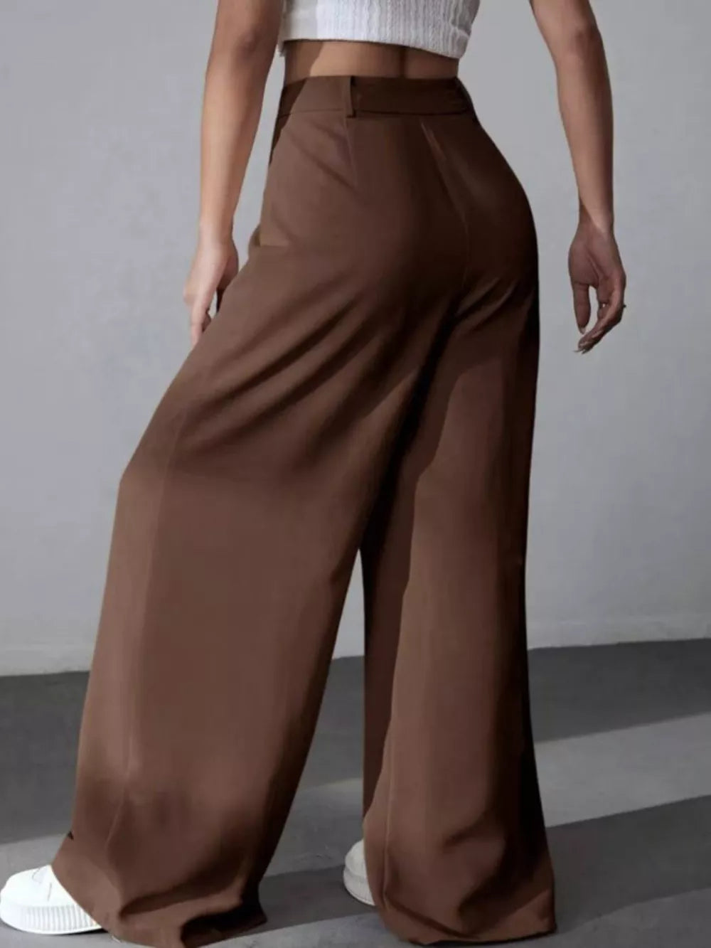 Brown high-waisted pleated wide-leg maternity trousers with a button closure.