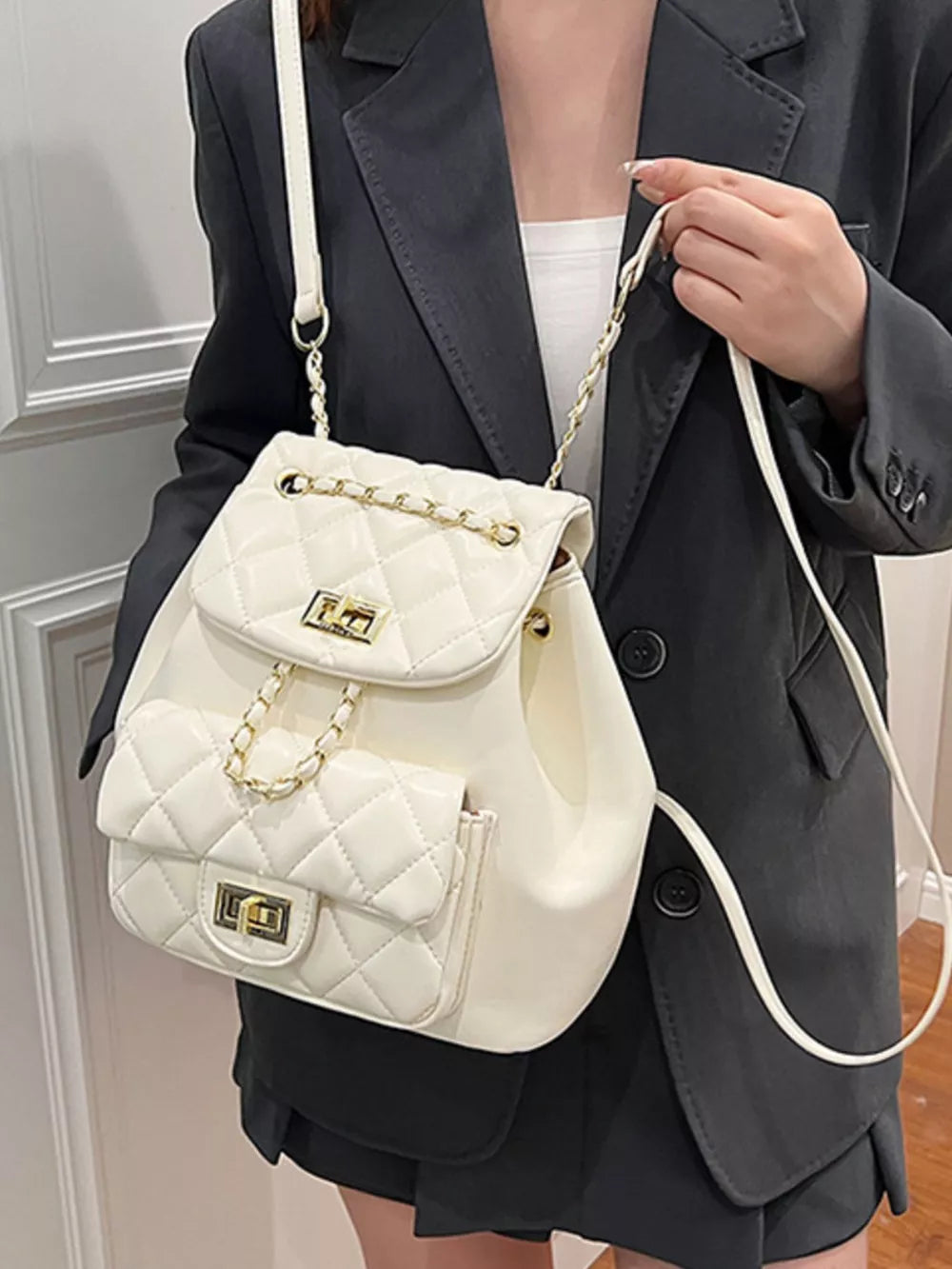 White quilted mini backpack with gold chain straps and front flap pocket.