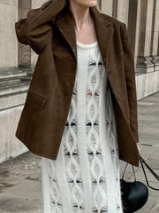 Brown suede blazer with structured shoulders and button closure, worn over a white distressed knit dress.