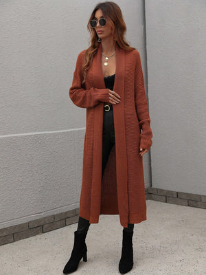 Brown textured knit maxi cardigan with open front and long sleeves, styled with a black top and boots.