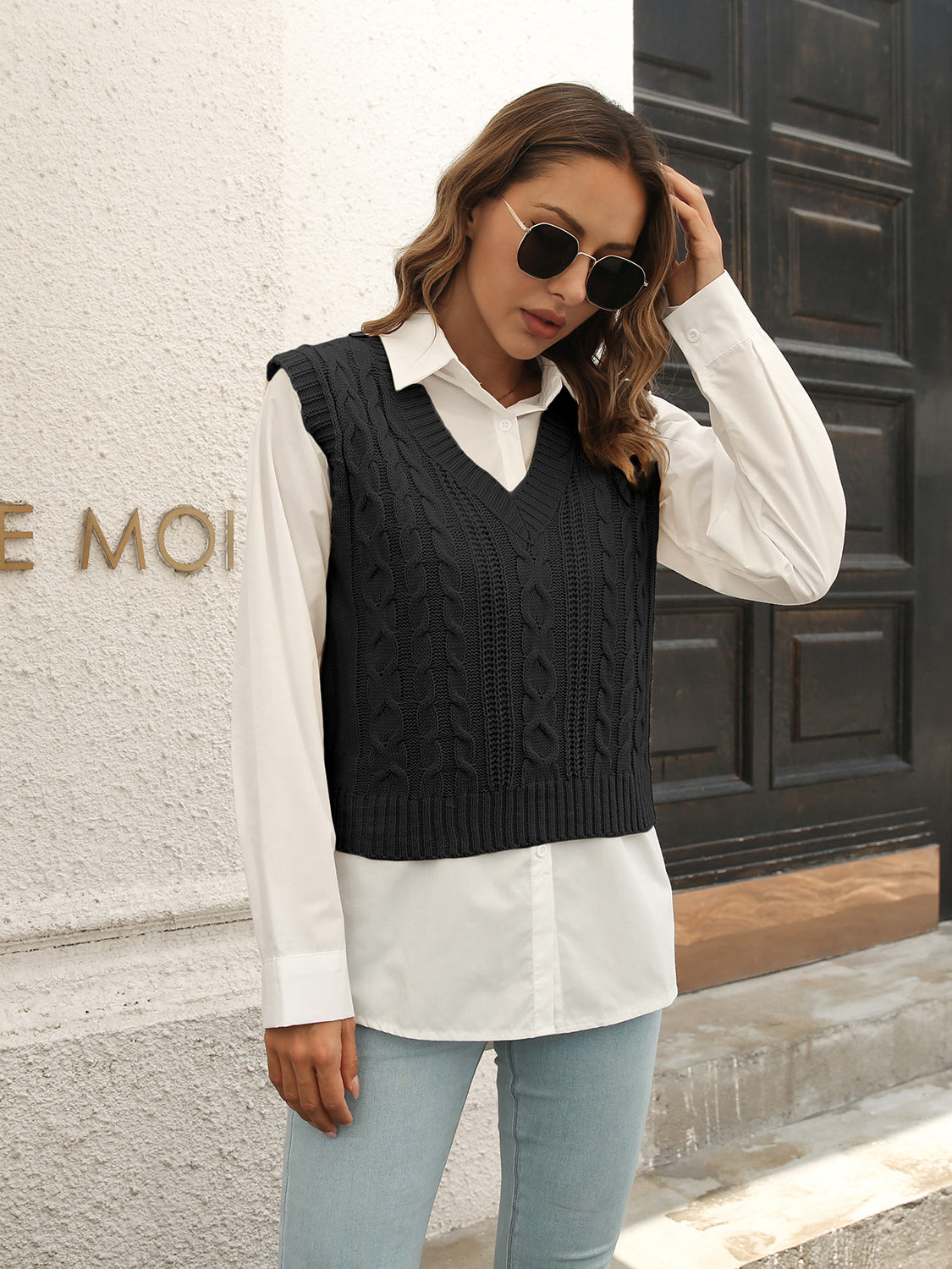 Black cable knit crop vest sweater with V-neck, styled over a white collared shirt.
