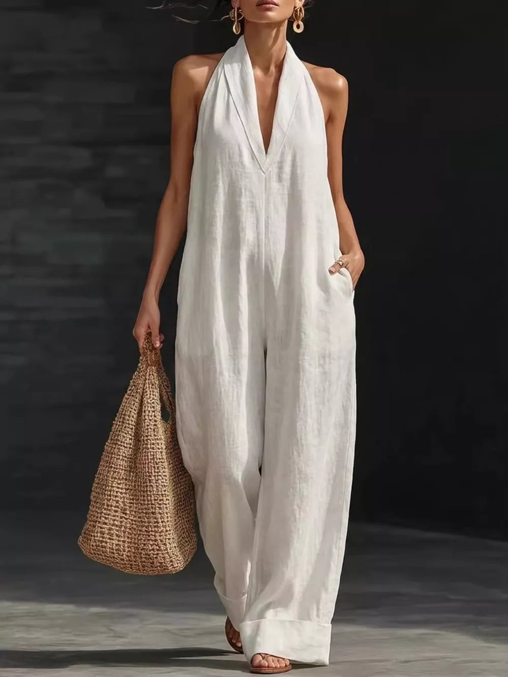 White halter neck wide-leg jumpsuit with deep V-neck and pockets, styled with a straw bag.