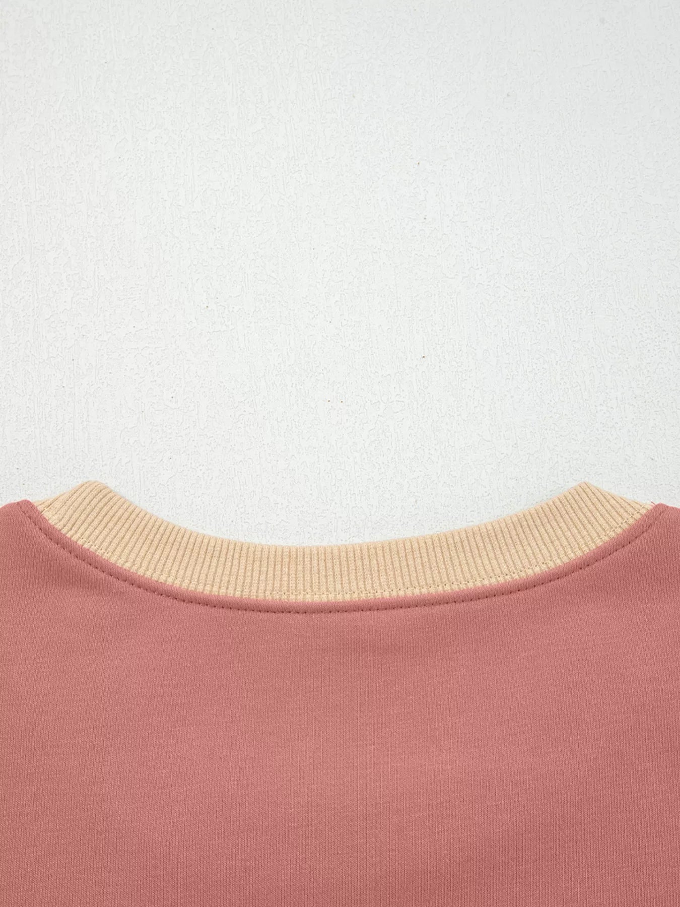 Dusty pink sweatshirt with contrast tan ribbed crewneck and exposed seams.