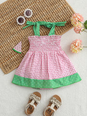 Smocked baby dress with pink gingham, green polka dot trim, and tie straps.