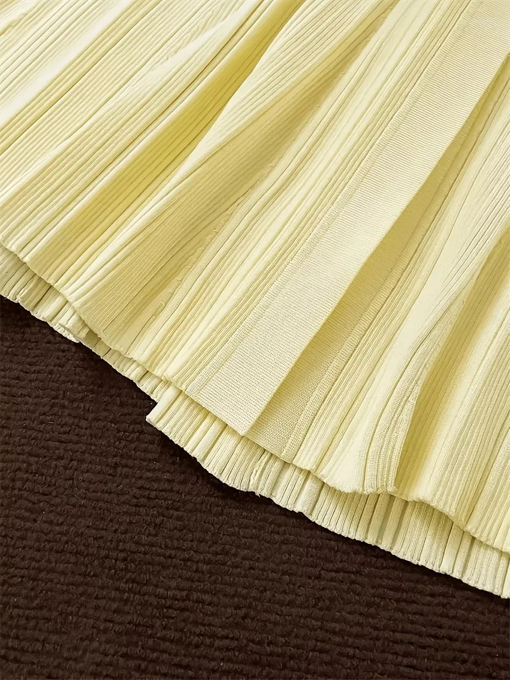 Pale yellow pleated knit sweater dress detail with ribbed texture and layered hem.