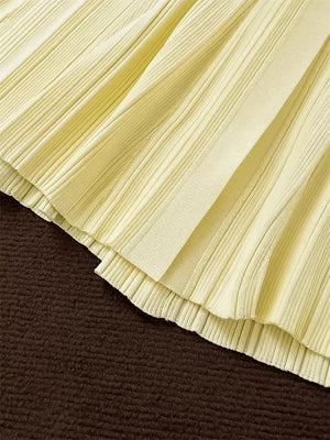 Pale yellow pleated knit sweater dress detail with ribbed texture and layered hem.