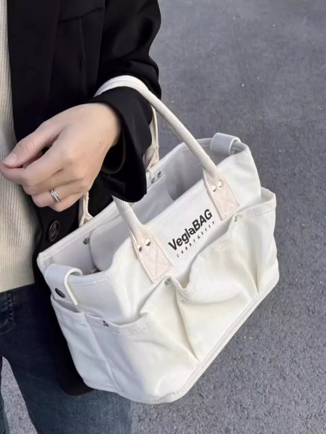 Beige canvas shopper bag with multiple exterior pockets and logo detail.