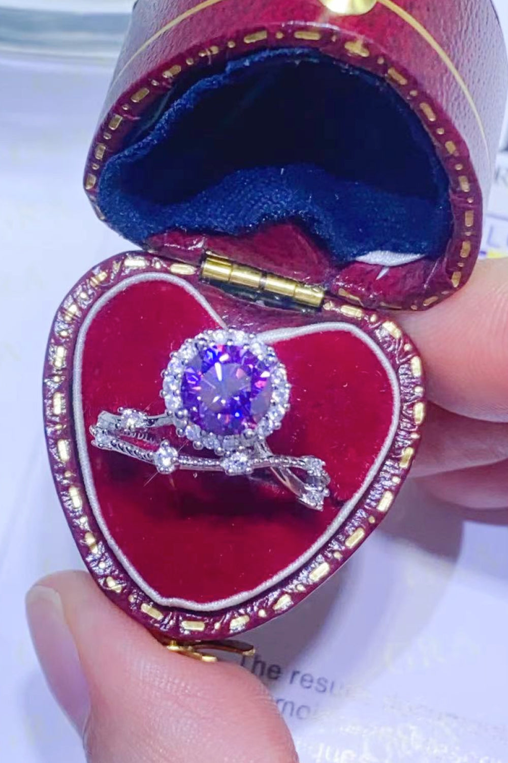 Purple moissanite engagement ring set with halo and diamond accents in a heart-shaped box