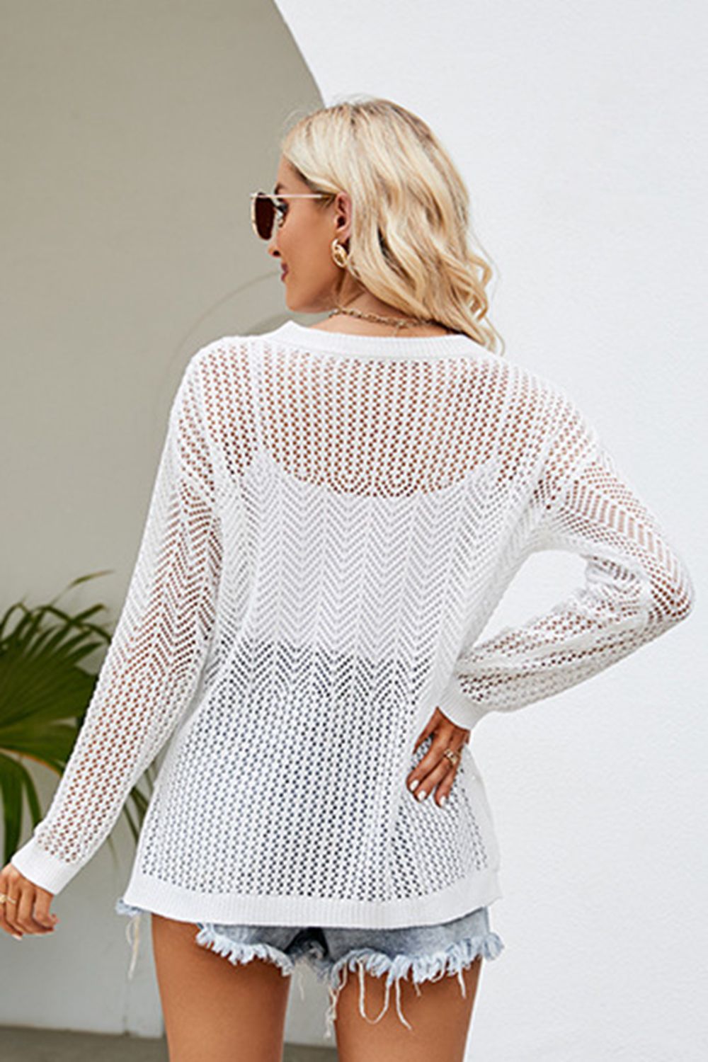 White openwork knit tunic with chevron pattern and long sleeves, styled with denim shorts.