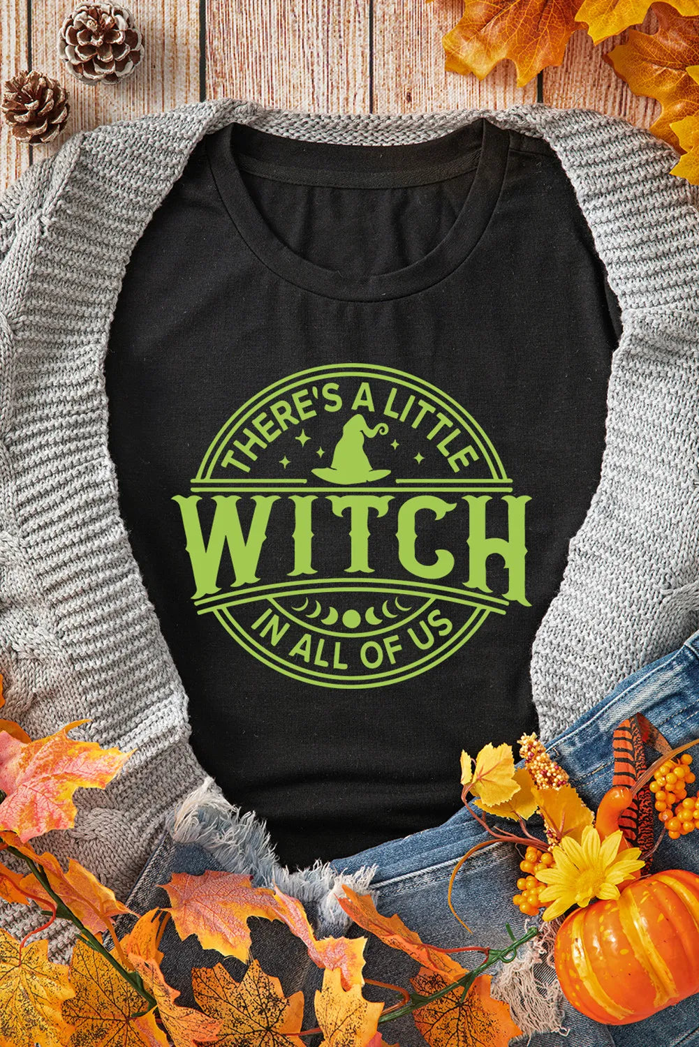 Black graphic t-shirt with a neon green witchy design that says "There's a little witch in all of us.