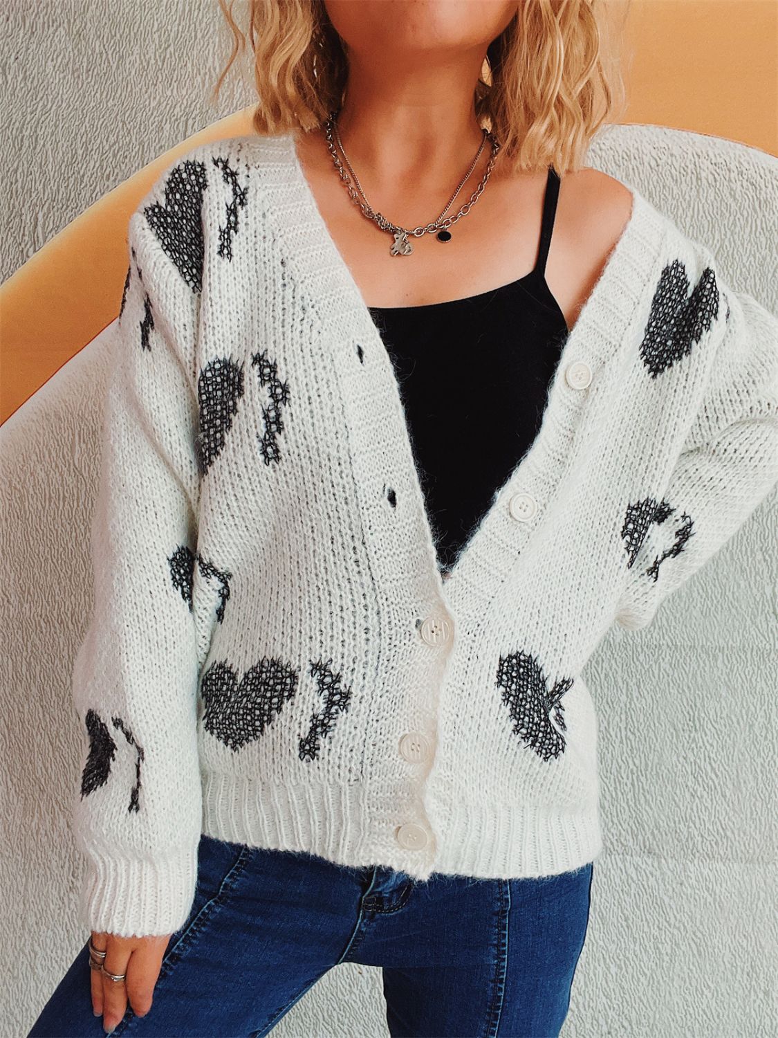 White knit cardigan with black heart motif, button front, V-neck, long sleeves.