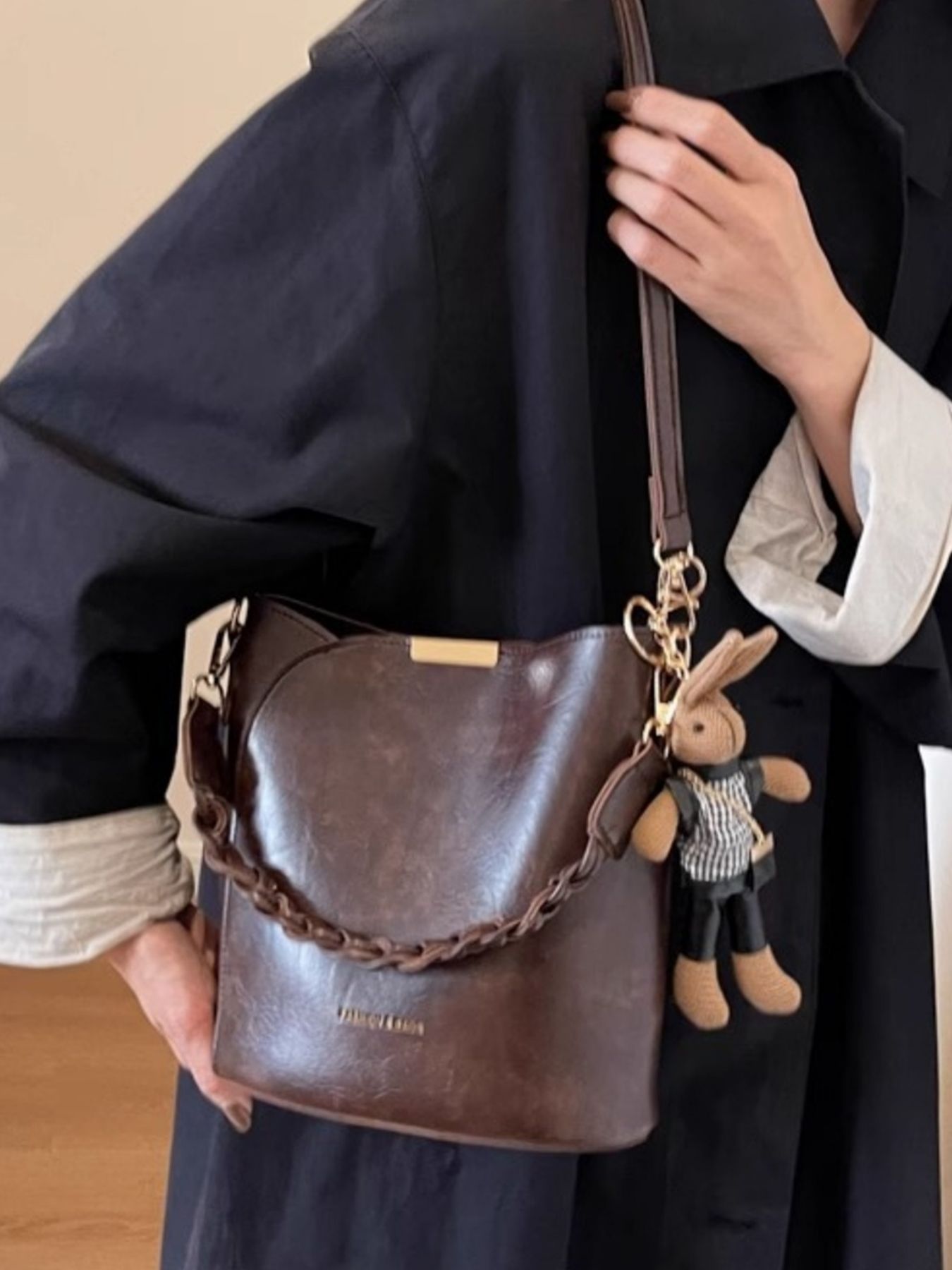 Brown braided bucket crossbody bag with bunny charm and gold hardware