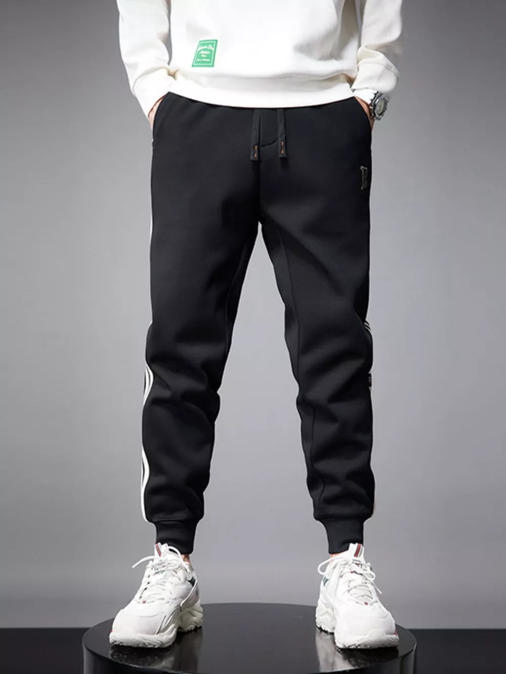 Black cotton joggers with white side stripes and cuffed ankles.